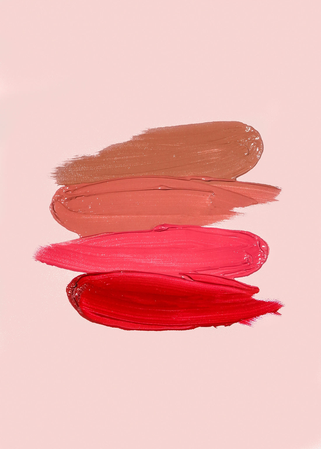 Four horizontal smears of lipstick in shades of brown, peach, pink, and red